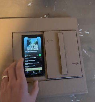 A cardboard prototype with a phone lying in the compartment and a sliding hatch